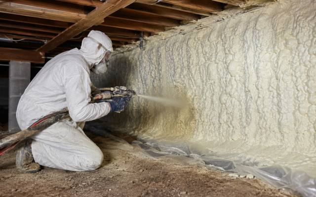 Installer sealing a crawl space wall with spray foam above a taped ground sheet